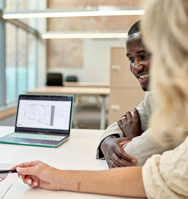 Two people discussing a building plan at a table with a laptop.