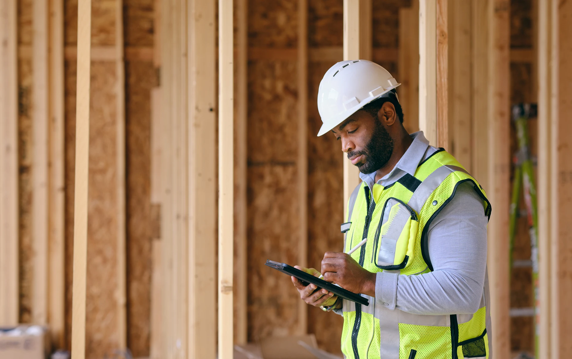 Construction worker wearing a hard hat and safety vest using a tablet at a job site