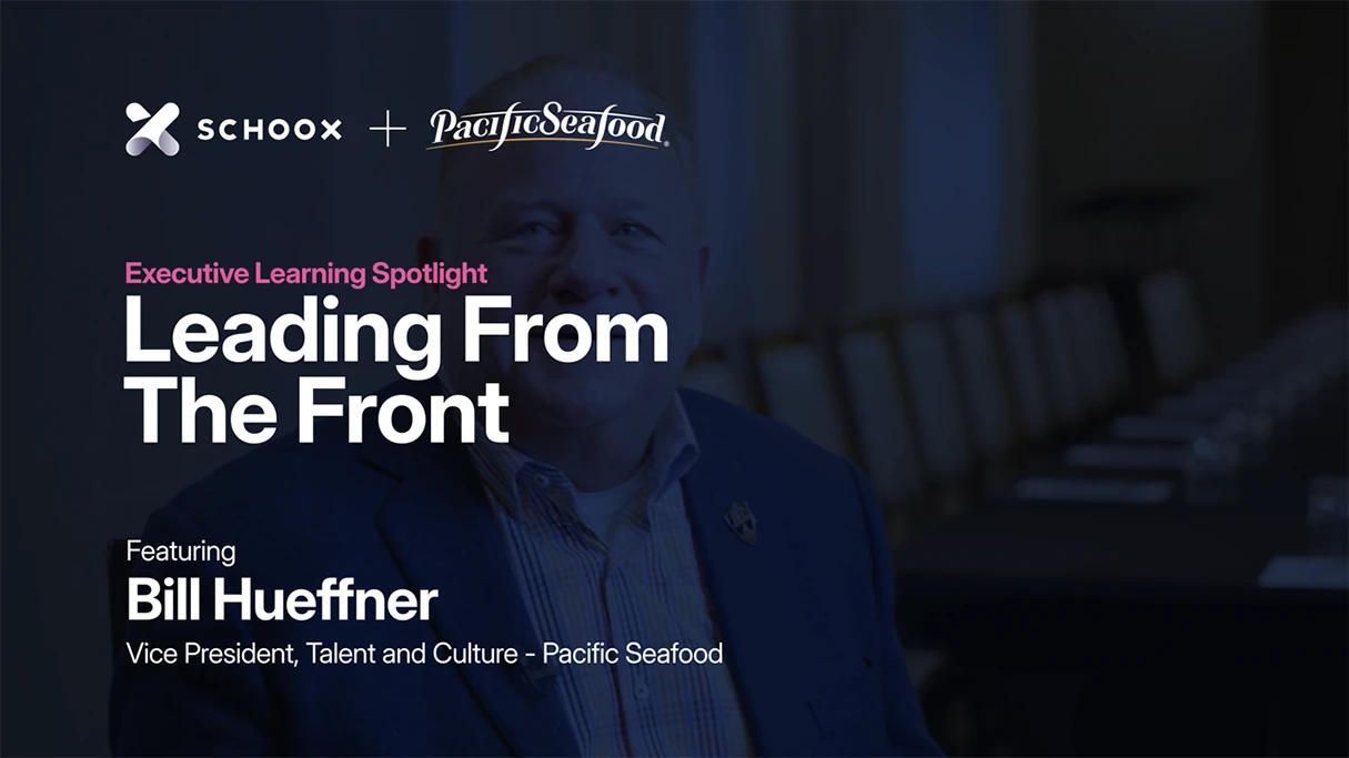 A man with a blue blazer smiles, promoting an executive learning series by Schoox and Pacific Seafood.