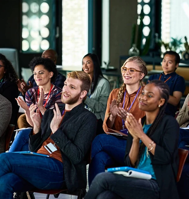 A diverse group of people applauding in a meeting room, engaged and smiling.