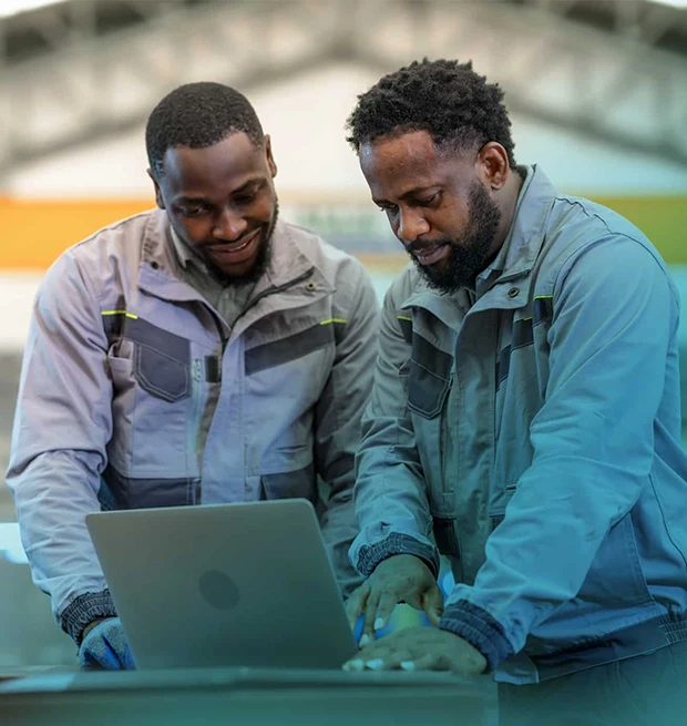 Two men in gray work jackets looking at a laptop, smiling and discussing.