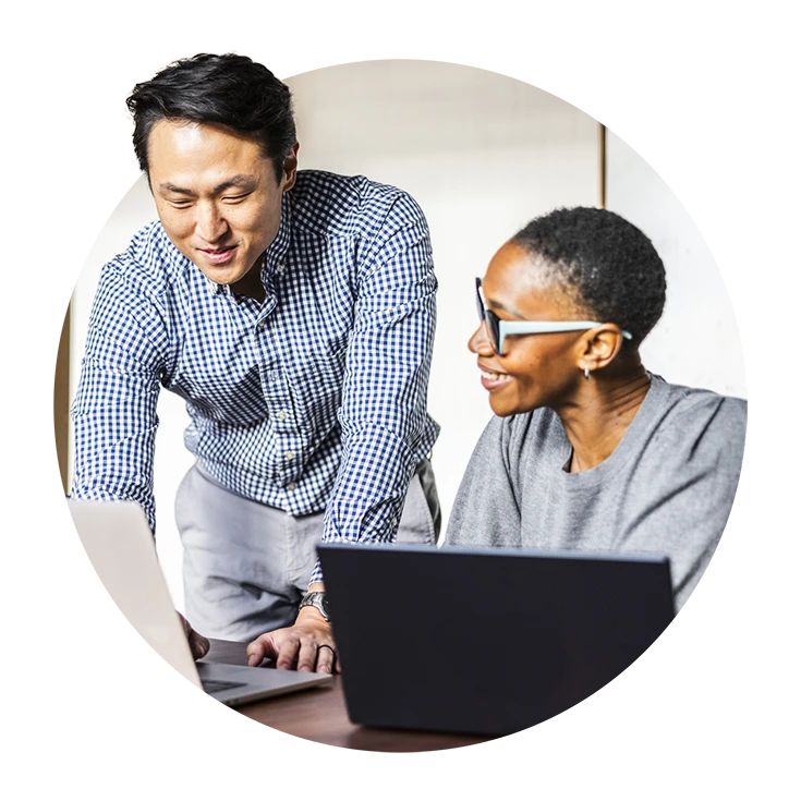 A man in a checkered shirt and a woman in glasses smile while discussing over a laptop.