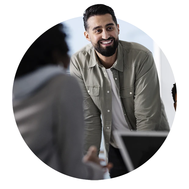 A smiling man with a beard in a casual outfit collaborates with others at a meeting.