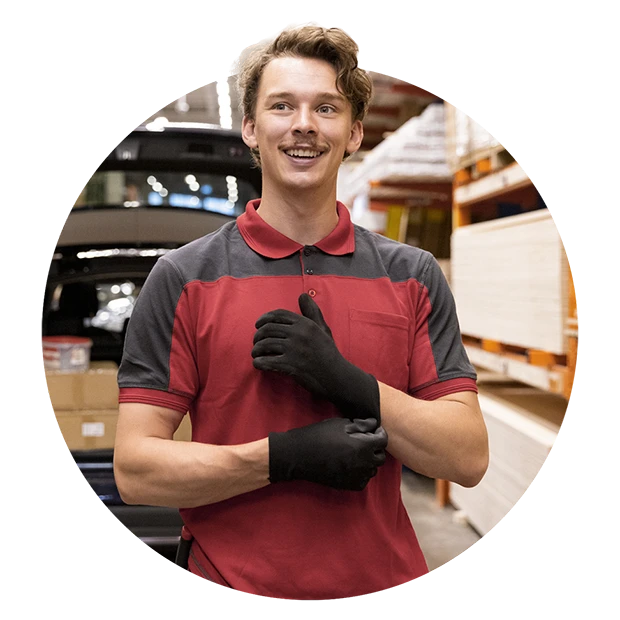 A smiling man in a red and gray shirt wearing black gloves in a warehouse setting.