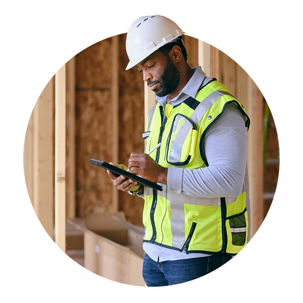A man in a hard hat and reflective vest using a tablet on a construction site.